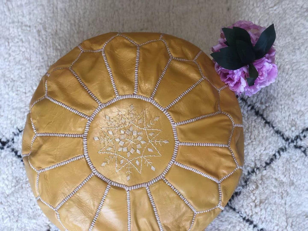 Handmade light yellow Moroccan leather pouf with embroidery on textured rug, pink flowers nearby