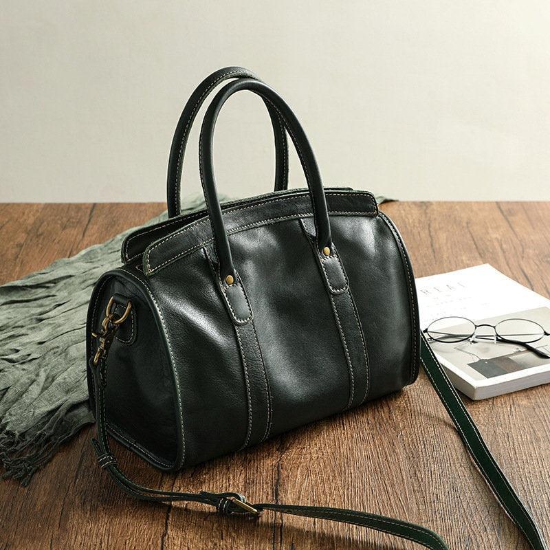 Black cowhide leather handbag with shoulder strap on wooden table, elegant and spacious design
