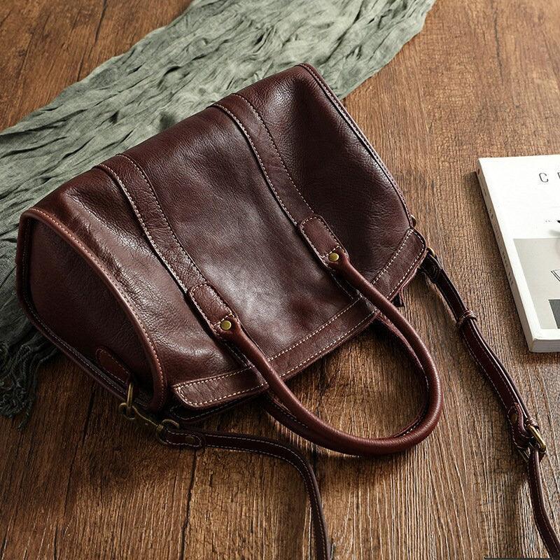 Large brown cowhide leather handbag with double handles and shoulder strap on wooden surface