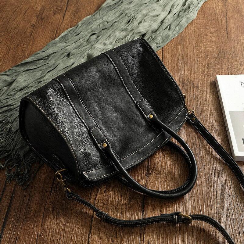 Large black cowhide leather handbag with shoulder strap on wooden surface