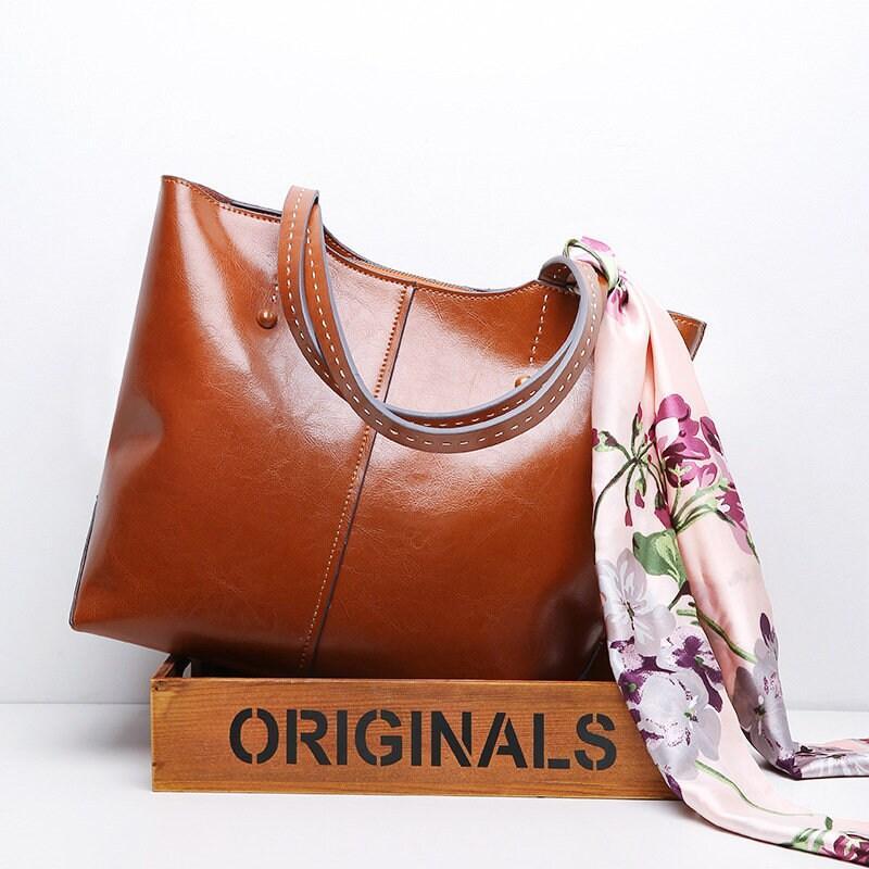 Brown leather tote bag with floral scarf draped over handle, displayed in wood crate
