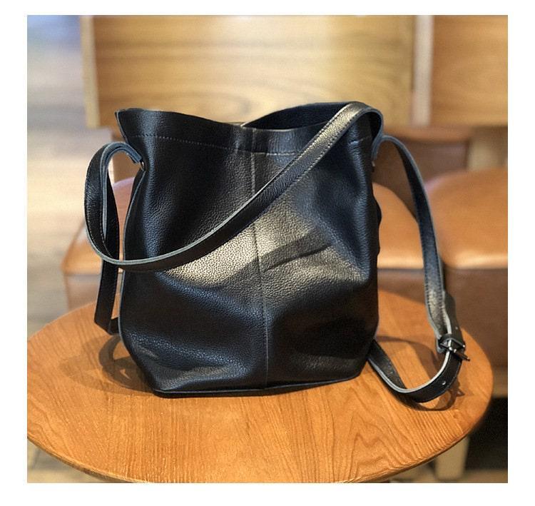 Black leather bucket bag with adjustable shoulder strap on a wooden chair