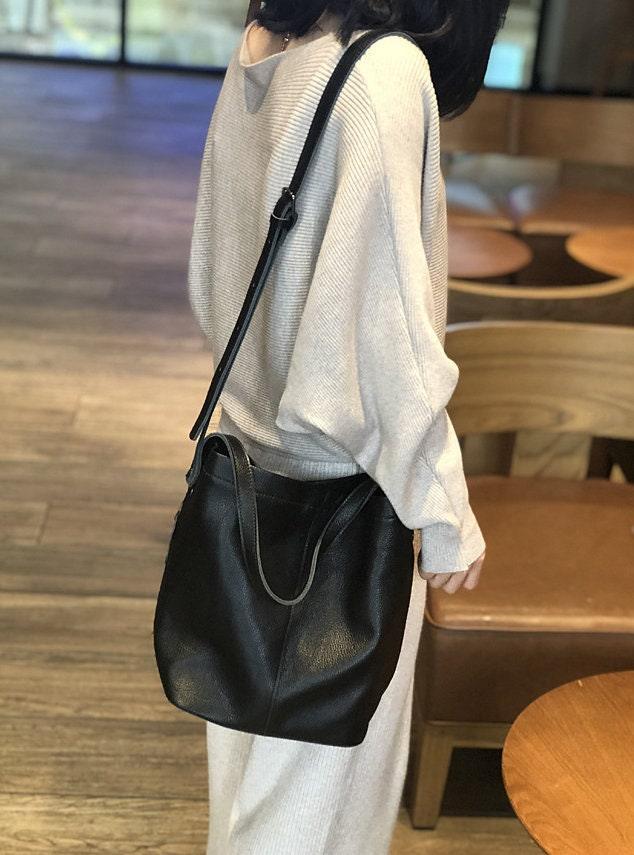 Woman wearing black leather bucket bag crossbody in casual indoor setting