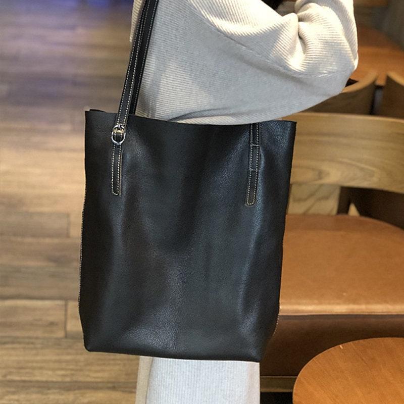 Large black leather tote bag with shoulder straps, shown on person indoors