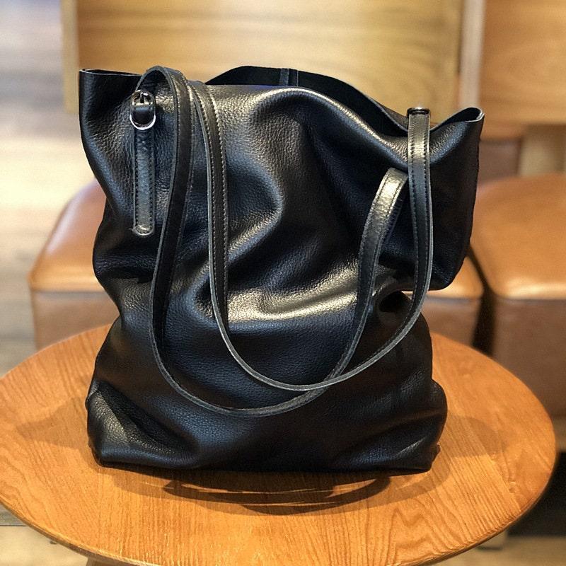 Large black leather tote bag with shoulder straps on a wooden table