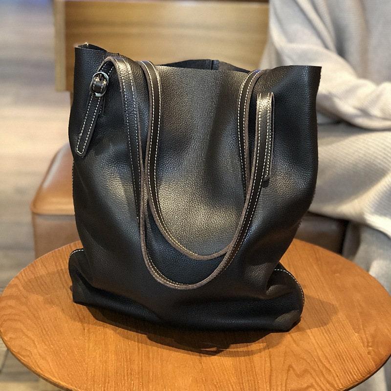 Large black leather tote bag with double handles on a wooden table, modern minimalist design