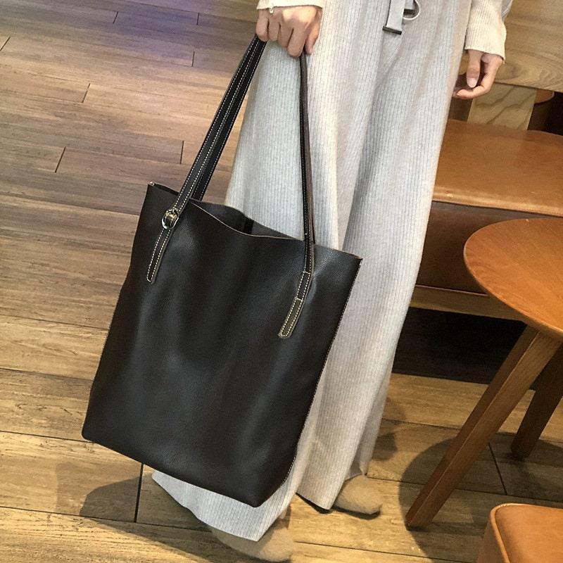 Large black leather tote bag with double shoulder straps, held by a person indoors