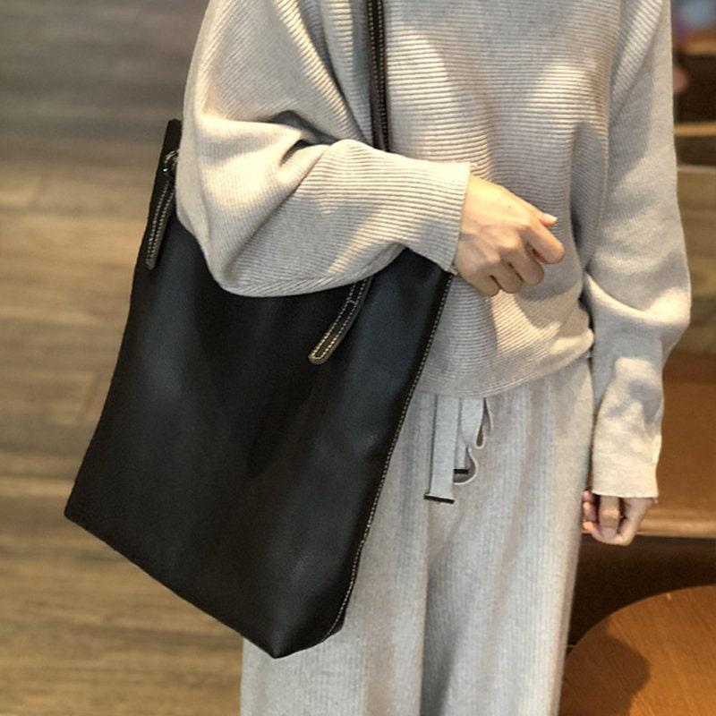 Woman carrying large black leather tote bag on shoulder, casual indoor setting