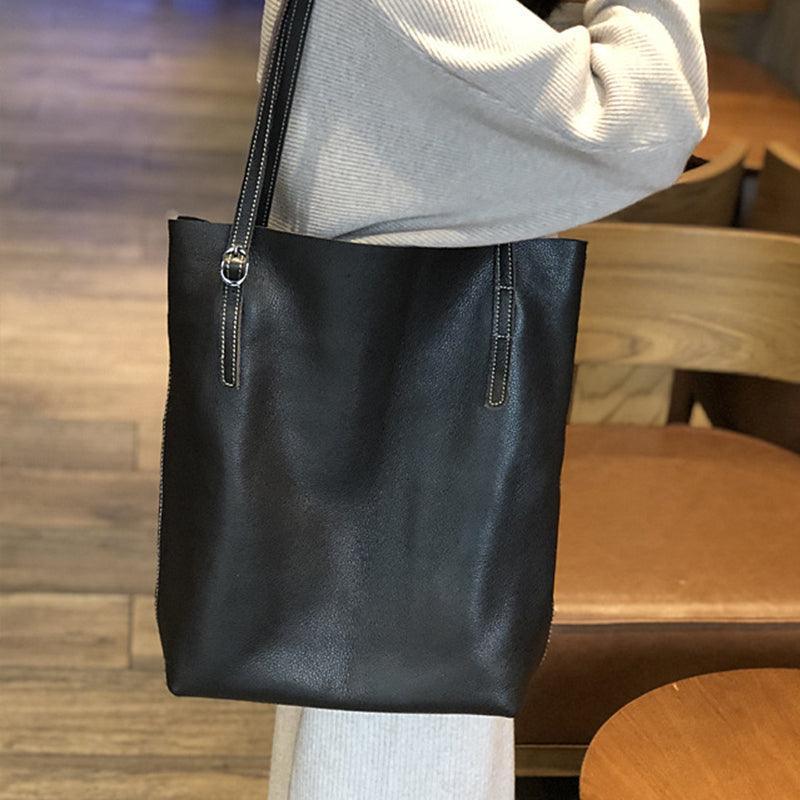 Large black leather tote bag with shoulder straps, held by a person indoors