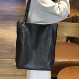 Large black leather tote bag with shoulder straps, held by a person indoors