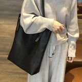 Oversized black leather tote bag with zipper detail, worn crossbody by woman in casual sweater.