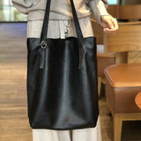 Oversized black leather tote bag with long straps, worn over the shoulder in a casual indoor setting