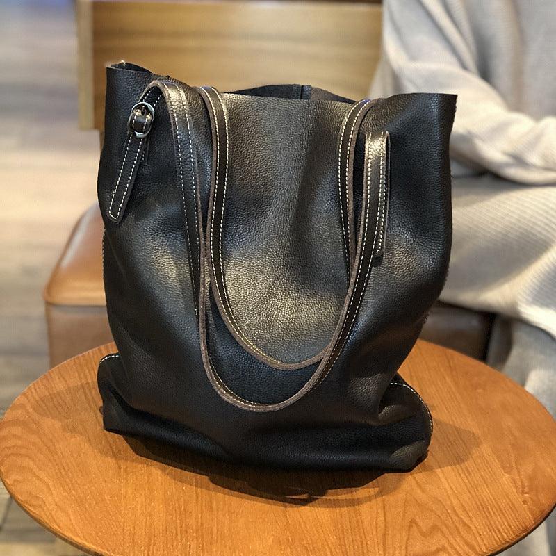 Oversized black leather tote bag with double handles on a wooden table indoors