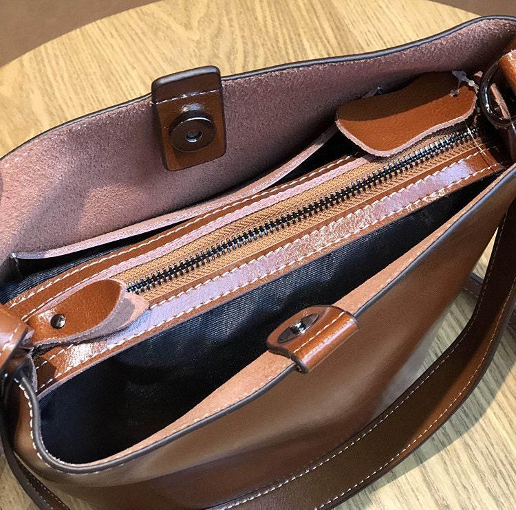 Brown leather bucket bag with zipper and magnetic closure on wooden table