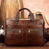Brown leather laptop shoulder bag with dual zip pockets, handles, and detachable strap, on wooden table
