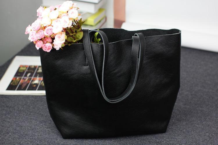 Large black full-grain leather tote bag with double handles on a gray surface, flowers inside