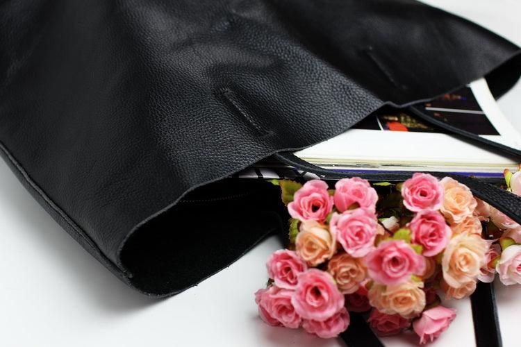 Black full grain leather tote bag with books and pink flowers inside, on white background.