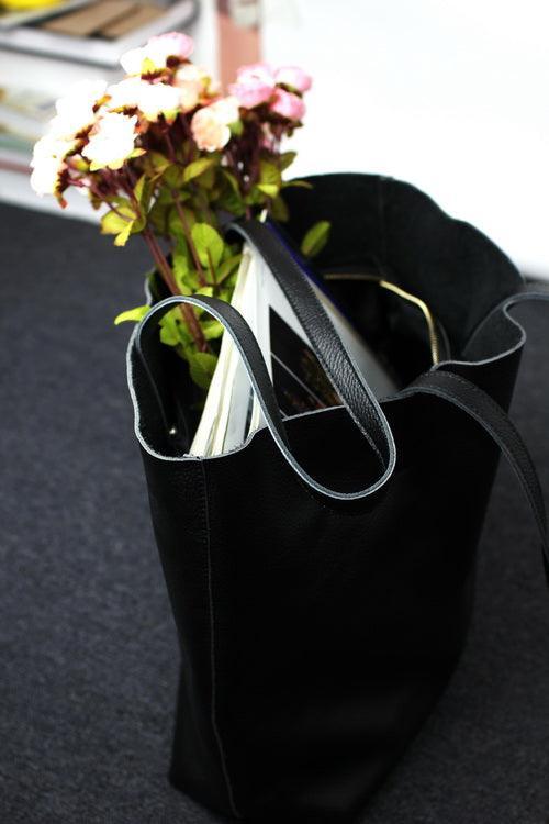 Black full grain leather tote bag with books and pink flowers inside on a dark surface