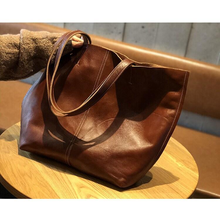 Brown minimalist leather tote bag with double handles on a round wooden table