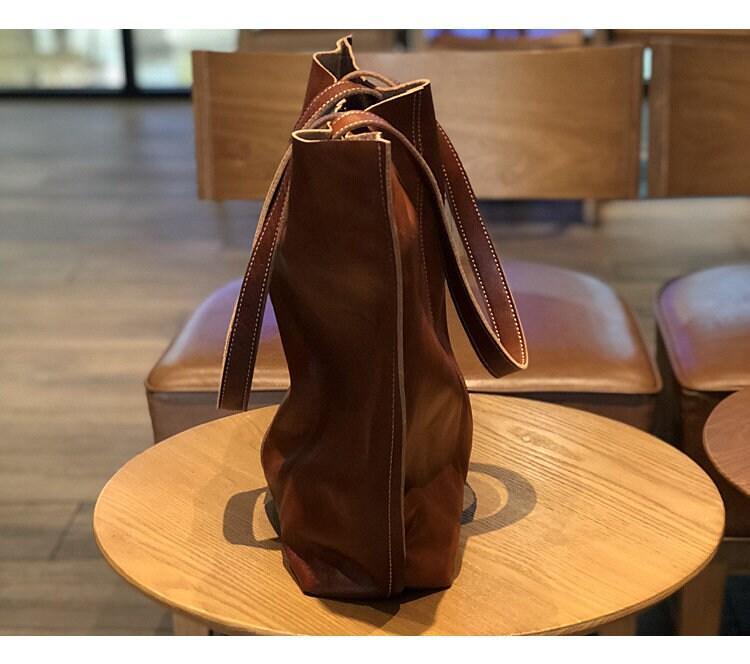 Side view of a large brown minimalist leather tote bag with white stitching on a wooden table