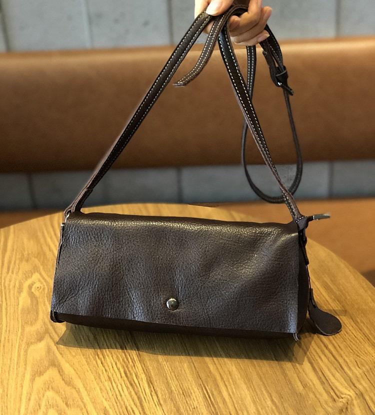 Minimalist small leather crossbody bag with flap and snap closure on wooden table