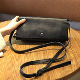 Minimalist small black leather crossbody bag with long strap on wooden table