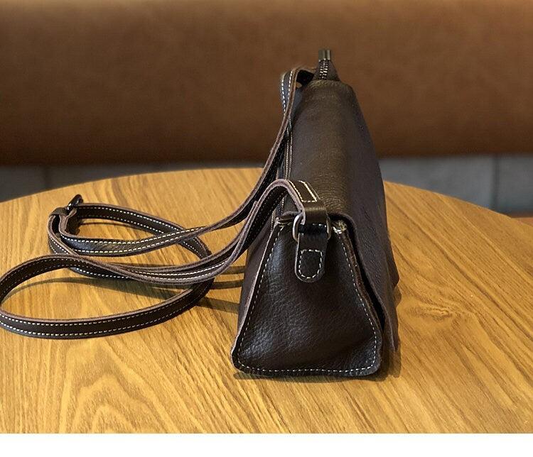 Minimalist small black leather crossbody bag with adjustable strap on wooden table