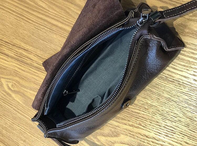 Open small black leather crossbody bag with zipper, interior pocket, on wooden surface