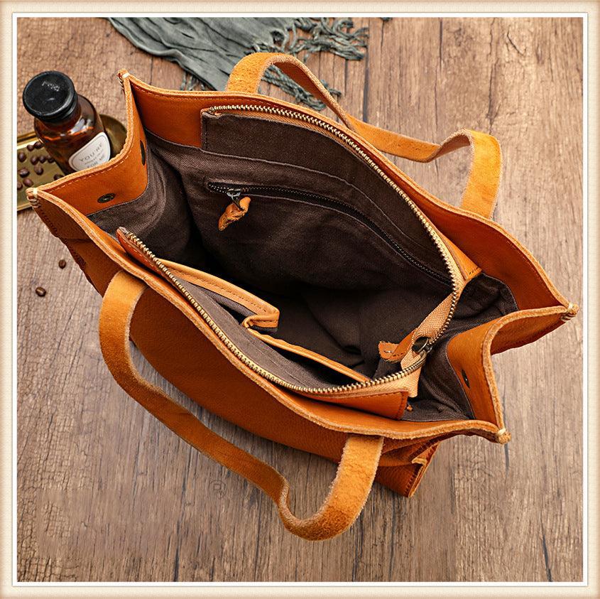 Open tan cowhide leather tote handbag with brown fabric lining and interior zip pockets on wood surface
