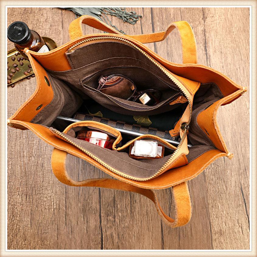 Open tan cowhide leather tote handbag with organized compartments, holding accessories inside
