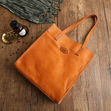 Natural tan cowhide leather tote handbag with shoulder straps on rustic wooden surface