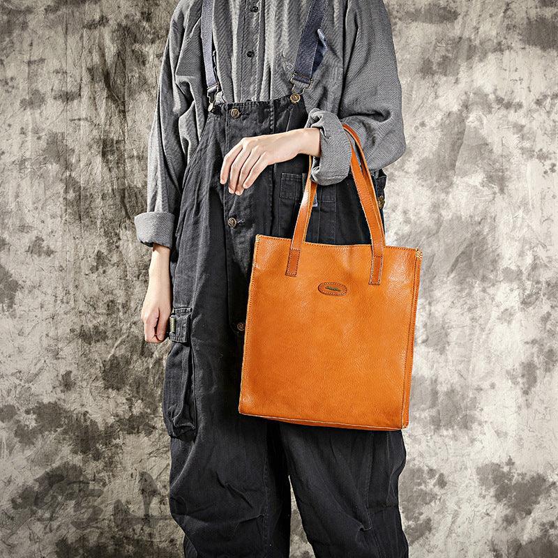 Woman holding a natural tan cowhide leather tote handbag with shoulder straps