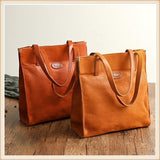 Two natural cowhide leather tote handbags with shoulder straps on wooden surface