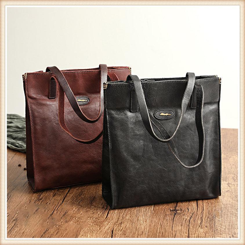 Brown and black cowhide leather tote handbags with shoulder straps on a wooden table