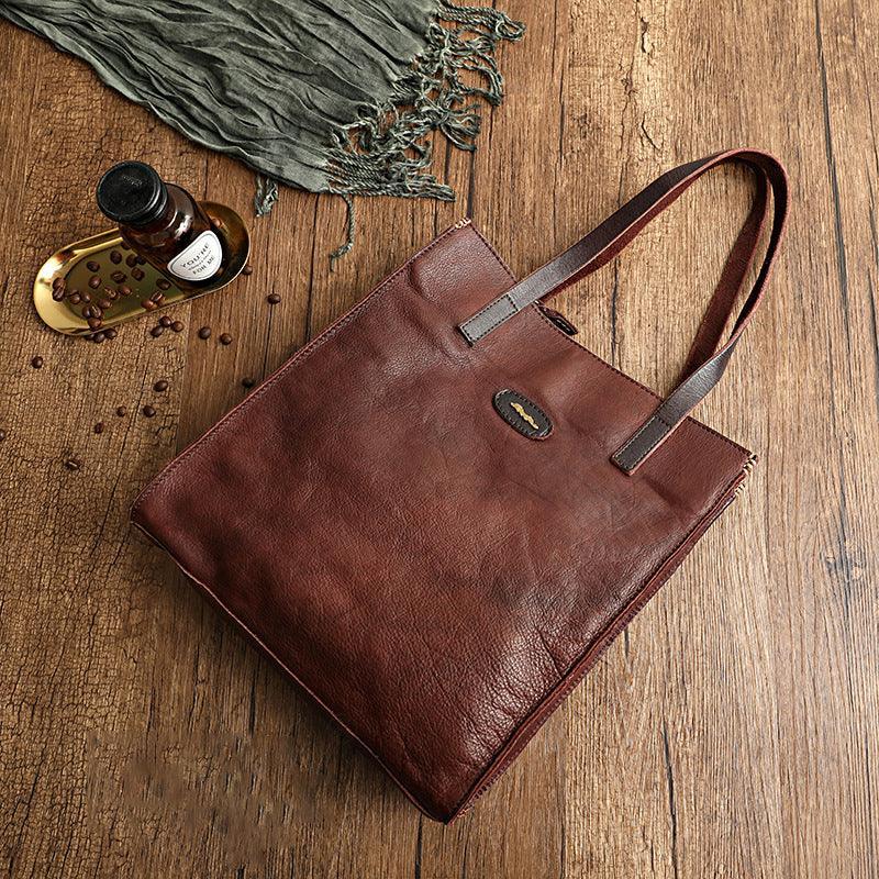 Brown cowhide leather tote handbag with shoulder straps on wooden surface