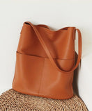 Brown cowhide leather tote bag with two front pockets and shoulder strap on woven surface