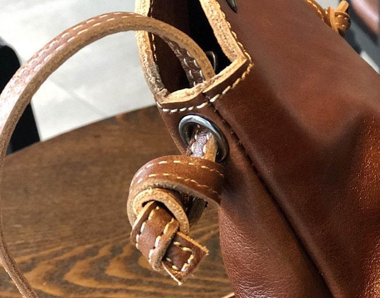 Close-up of small genuine tanned leather crossbody bag with knotted strap and stitched edges