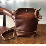 Small genuine leather crossbody shoulder bag with tan stitching on a wooden table