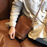 Small brown genuine leather crossbody shoulder bag with retro design on a person's lap