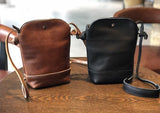 Brown and black genuine leather small crossbody shoulder bags with snap closures on a wooden table