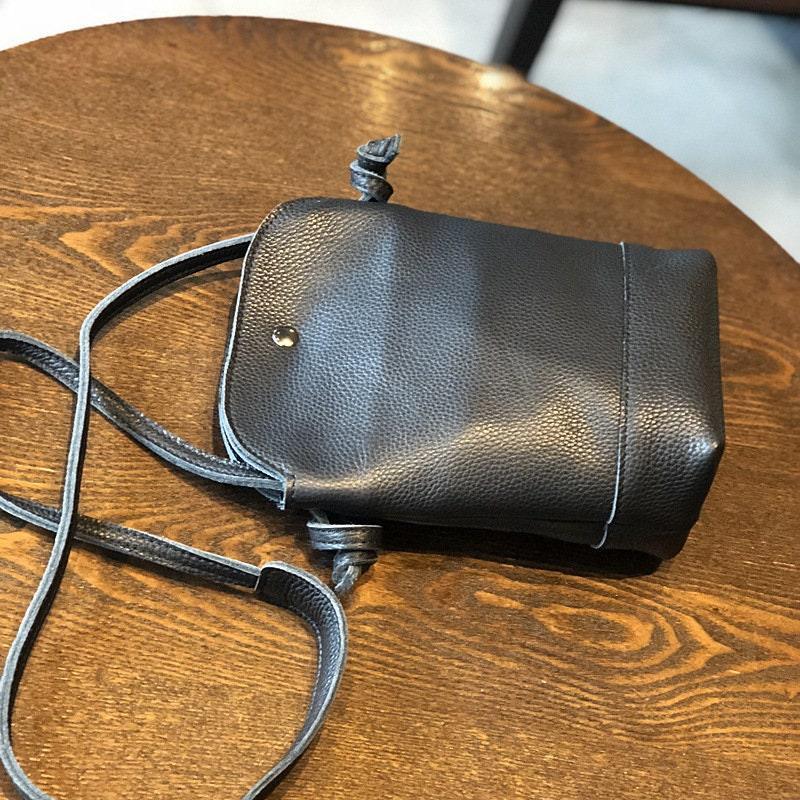Small black genuine leather crossbody bag with adjustable strap on wooden table