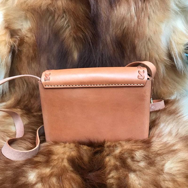 Small handcrafted leather shoulder bag with crossbody strap on a fur background