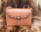 Small handcrafted leather shoulder bag with stitched flap and brass button, on fur background