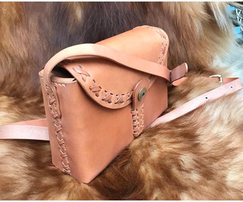 Small handcrafted tan leather shoulder bag with braided stitching on fur background