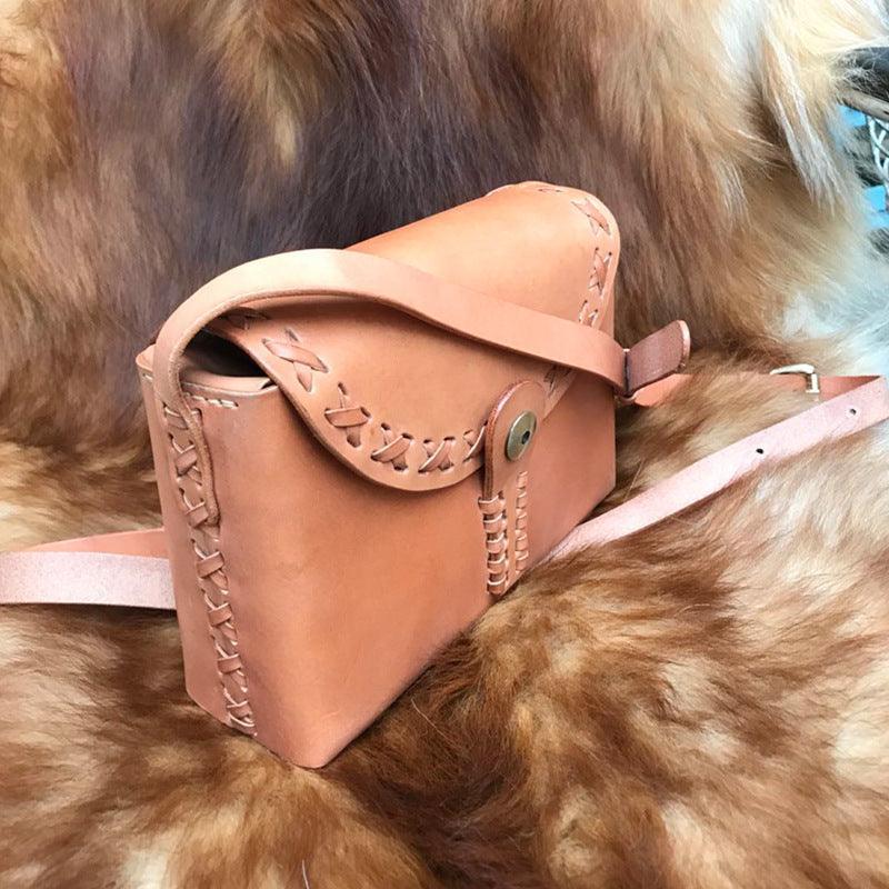 Handcrafted tan leather shoulder bag with stitched edges on a fur background