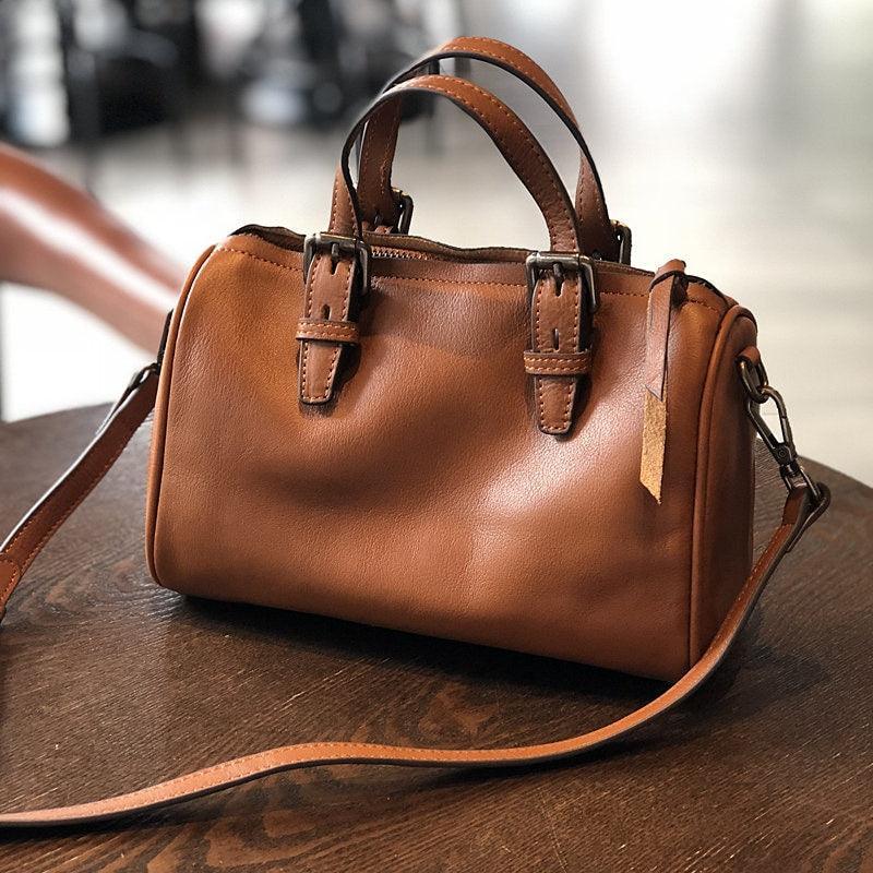 Small vintage brown leather Boston bag with shoulder strap and buckle handles on a table