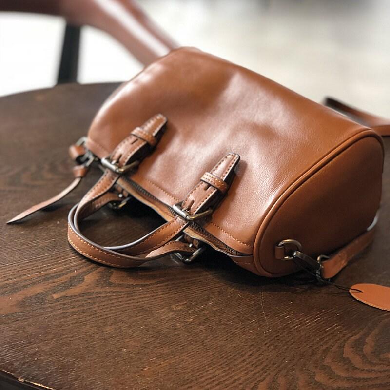 Small vintage brown leather Boston bag with buckled handles on a wooden table