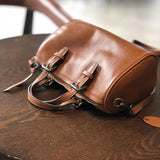 Small vintage brown leather Boston bag with buckled handles on a wooden table