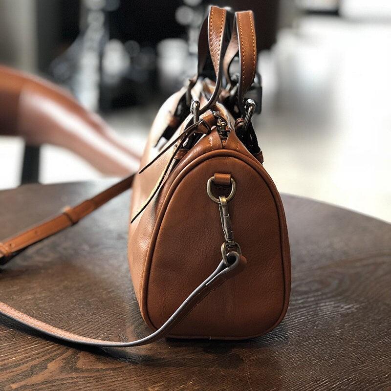 Small vintage brown leather Boston crossbody bag with shoulder strap on a wooden table