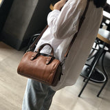 Small vintage brown leather Boston crossbody bag with top handles worn over shoulder